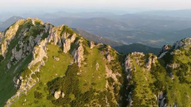 Bir hava videosu engebeli bir dağ zirvesine doğru sinematik bir hareket yakalar. Görüntülerde kayalık tepeye çıkan önemli bir yürüyüş yolu görülüyor. Sahne engin bir dağda geçiyor.