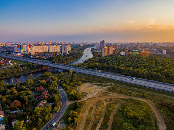  Drone view of a summer sunset on a river and highway over an urban environment with a blue sky.