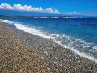 Dağ ve deniz manzaralı bir çakıl taşı plajında mavi gökyüzü olan deniz burnu.