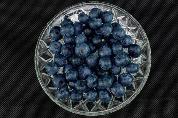 Fresh blueberries in a crystal bowl on a black background.