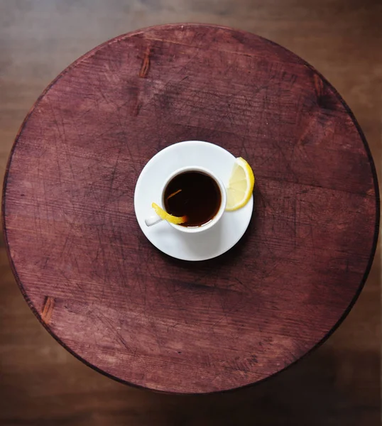 Espresso romano coffee with lemon in a white cup on a round dark wooden rustic table top view