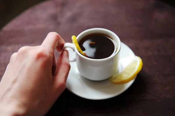 Espresso romano coffee with lemon in a white cup on a dark wooden rustic table. Hold in hand closeup
