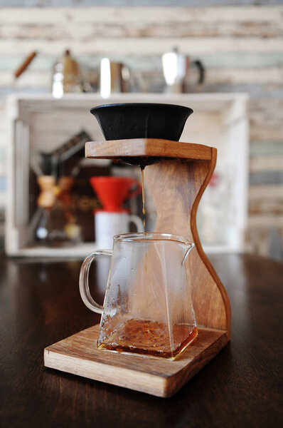 Изготовление кофе в черной безбумажной пористой керамической фарфоровой фильтр на деревянной кофейной станции. Устройства для пивоварения на заднем плане
