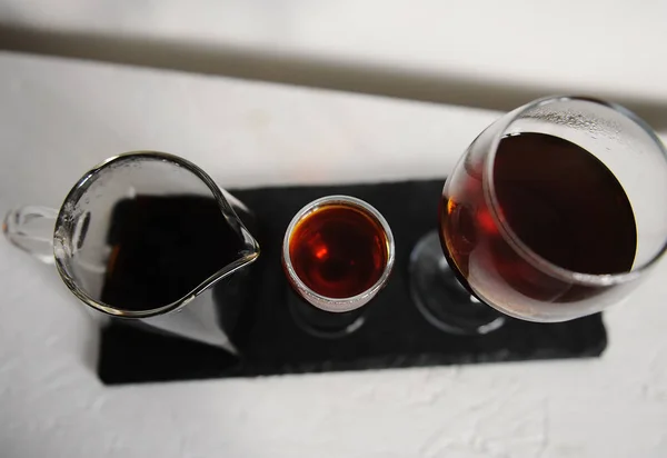 Coffee in a transparent serving teapot of two wine glasses for tasting. Served on a slate board on a white background. — Stock Photo, Image