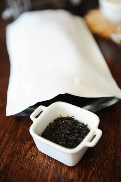 Tasarımı için ücretsiz yer beyaz ambalajlı yakınındaki beyaz bir kase içinde çarpık siyah çay yaprakları — Stok fotoğraf