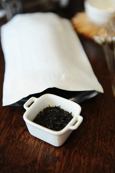 Twisted черный чай листья в белой миске рядом с белой упаковки с бесплатным местом для дизайна — стоковое фото