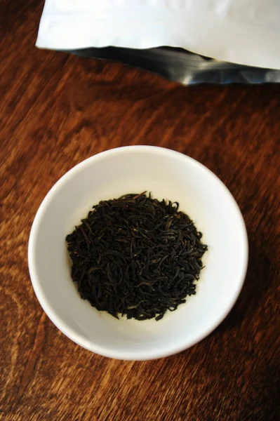 Tvinnade svarta teblad i en vit skål nära vita förpackningen med gratis plats att utforma — Stockfoto