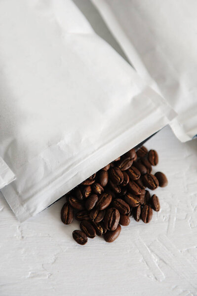 Крупным планом свежие жареные кофейные зерна, выливающиеся из открытого белого пакета на стол
