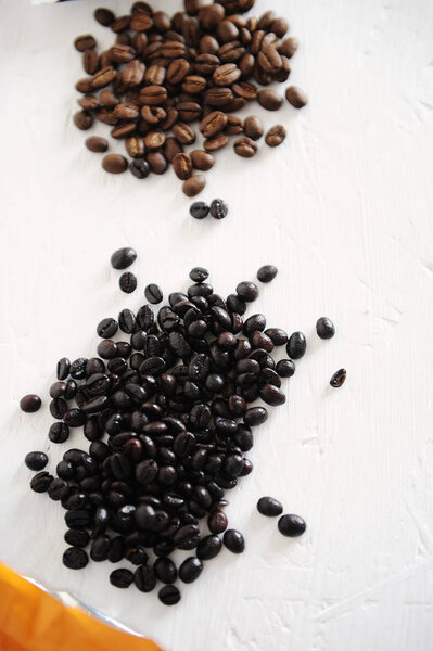 Два вида кофе обжига выливаются из пакетов для сравнения на белый стол. Темно-испанский жаркое torrefacto с сахаром и обычный легкий жаркое
