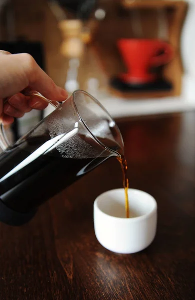 Рука наливает кофе из стакана в белый эспрессо без ручки — стоковое фото