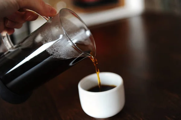 Hand gießt Kaffee aus einer Glaskanne in eine weiße Espressotasse ohne Henkel — Stockfoto