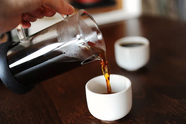 Verser à la main le café d'une cruche en verre dans une tasse à expresso blanche sans poignée — Photo