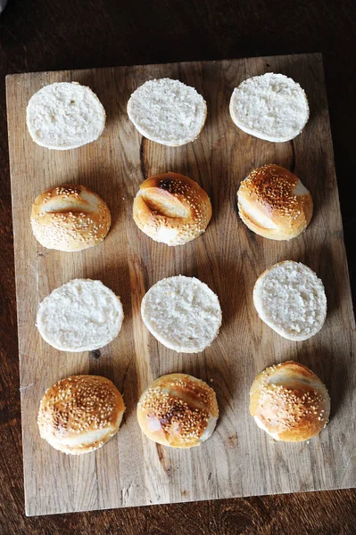 Bollos de hamburguesas de sésamo divididos por la mitad en la vista superior de tabla de cortar de madera. Proceso de cocción —  Fotos de Stock