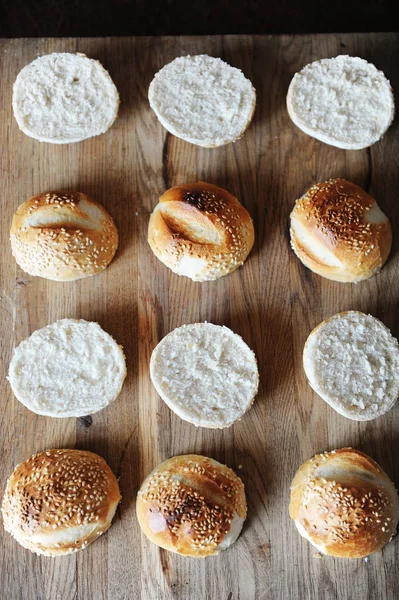 Sesame burgers buns split in half on wooden cutting board top view. Cooking process — Stock Photo, Image