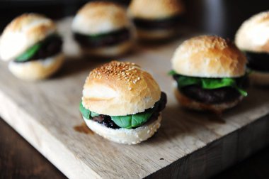 Bir ahşap tahta üzerinde altı taze pişmiş hamburger. Susam çörek, dana pirzola, ıspanak yeşil ve berry sos.