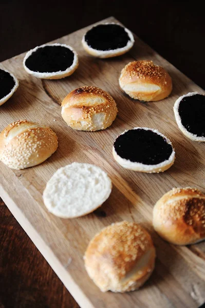 Bollos de hamburguesas de sésamo partido por la mitad en la tabla de cortar de madera. salsa de bayas oscuras en la parte superior. Proceso de cocción —  Fotos de Stock