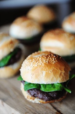 Bir ahşap tahta üzerinde altı taze pişmiş hamburger. Susam çörek, dana pirzola, ıspanak yeşil ve berry sos.