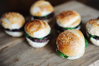 Bir ahşap tahta üzerinde altı taze pişmiş hamburger. Susam çörek, dana pirzola, ıspanak yeşil ve berry sos.
