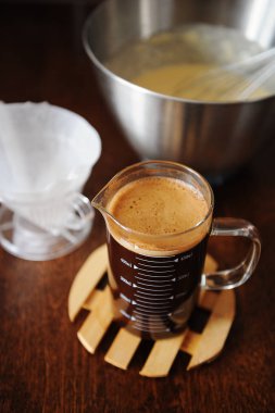 Kahve kek yapma. Çırpma teli ile kase hamur. Sürahi ve kağıt filtre kahve infüzyon. Koyu ahşap masa