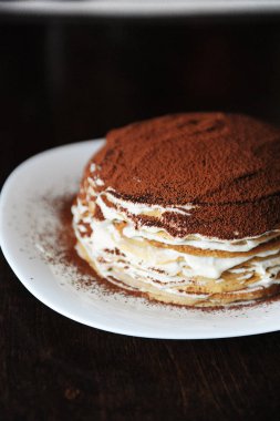 Taze pişmiş tiramisu krep pasta toz kakao ile silkeledi. Beyaz tabak, ahşap masa. Yarım pasta yakın çekim
