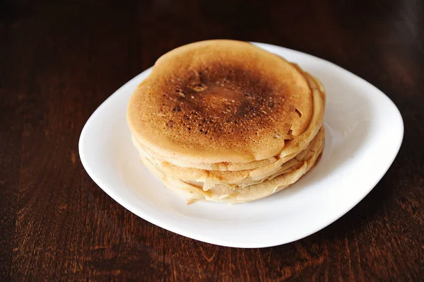 Uma pilha de panquecas em uma placa branca em uma mesa de madeira escura — Fotografia de Stock