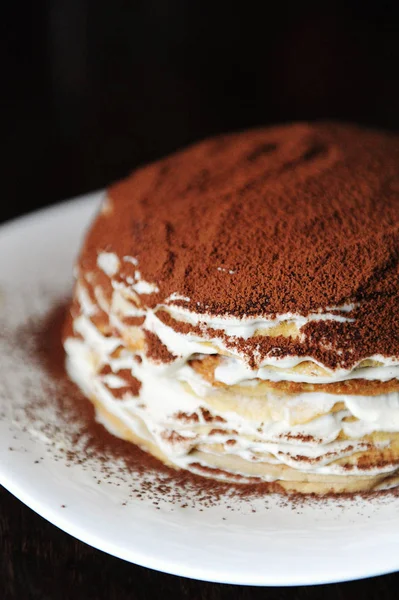 Frisch gekochter Tiramisu-Crêpe-Kuchen mit pudrigem Kakao bestäubt. weißer Teller, Holztisch vorhanden. halbe Torte aus nächster Nähe — Stockfoto