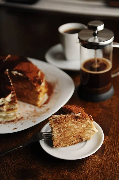 Piece of crepe cake with tiramisu filling and powdery cocoa is served on plate. The interior of coffee shop — Stock Photo, Image