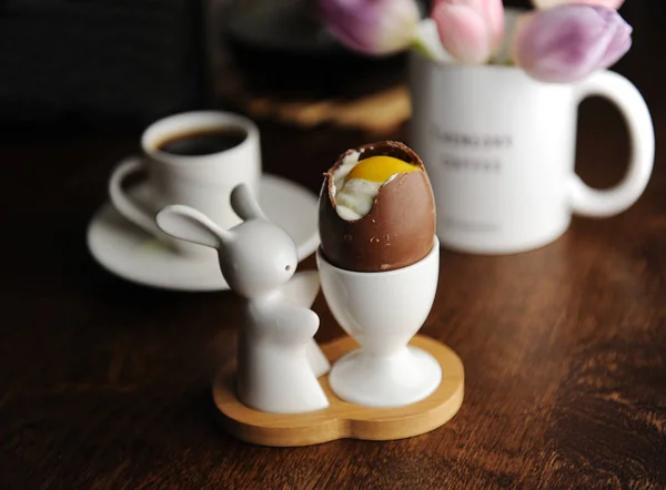 Easter dessert chocolate eggs filled with cream imitating white and yolk. Coffee cup. Served on holder with Easter bunny