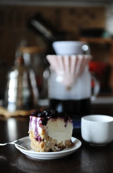 Et stykke blåbær cheesecake på en hvid plade side visning. Kaffe i origami dripper. Lækker dessert - Stock-foto