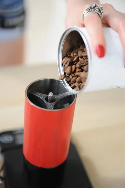 Barista menina derrama café foi de uma lata branca em um moedor de café manual vermelho de perto — Fotografia de Stock