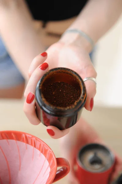 Свежемолотый кофе в стеклянном контейнере кофемолки крупным планом в женской руке с красными ногтями — стоковое фото