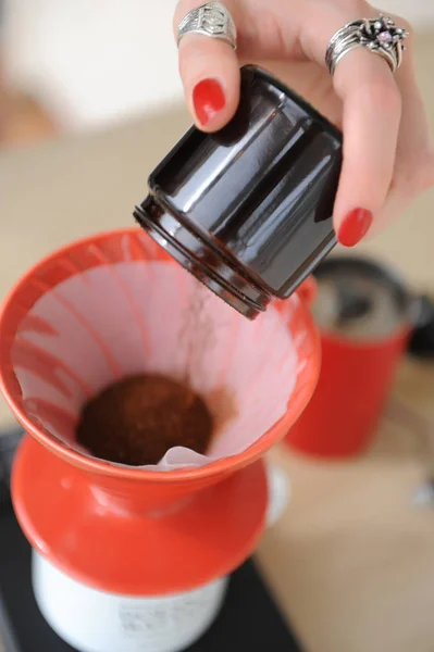 Chica barista vierte café recién molido de molinillo de café manual en una bolsa roja con filtro de papel de primer plano — Foto de Stock