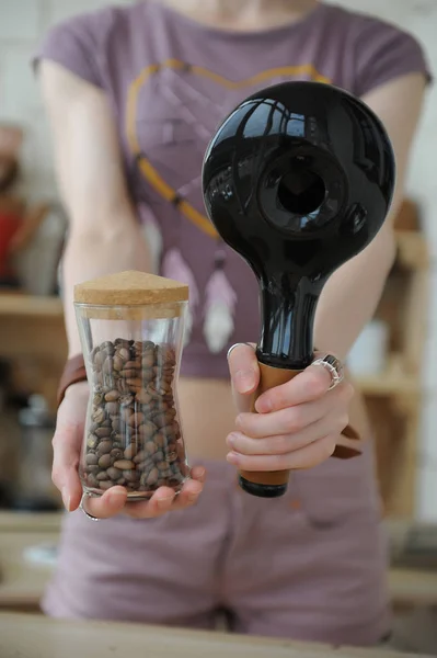 Chica sostiene en las manos tostadora de café muestra de cerámica y frasco de vidrio con granos de café recién tostados — Foto de Stock
