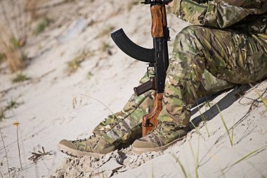 Askeri üniformalı erkeklere kum üzerine oturur ve bir tüfek ile onun ellerini tutar. Seçici odak