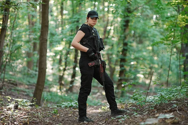 Woman with rifle in hands in black uniform in the forest.Selective focus