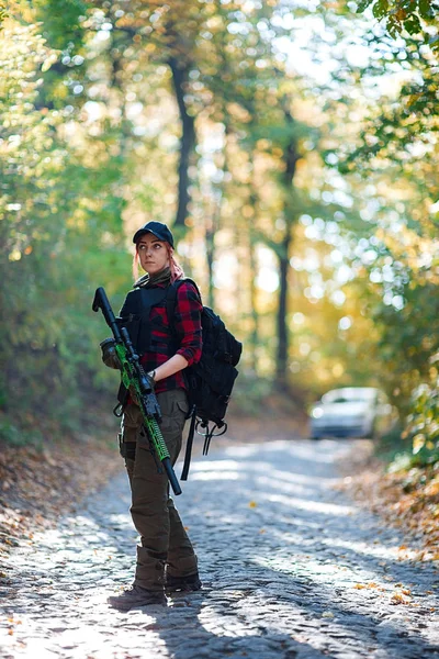 Woman with rifle in the forest. Car in the background/Red-haired young woman with a rifle on the road in the forest. Car in the background