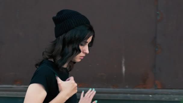 A young girl walks cautiously, looking around and leaning against an old rusty wall — Stock Video