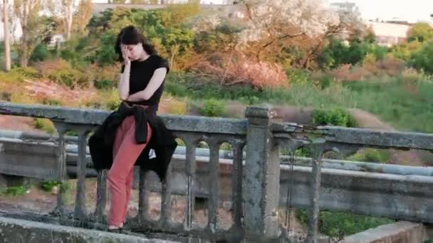 A view from right to left of a sad woman, standing on a bridge, who sadly covers her face with hands and starts — Stock Video