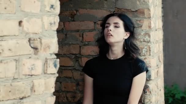 A view from left to righ of a young woman, leaning against a wall, sighing and disarranging her hair — Stock Video