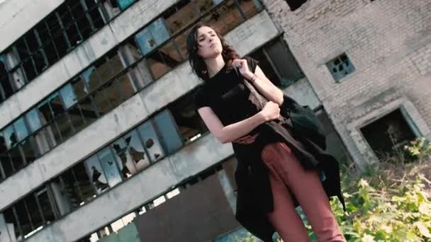Μια νεαρή γυναίκα στέκεται ενάντια σε ένα εγκαταλειμμένο κτίριο και αναρωτιέστε όπου είναι — Αρχείο Βίντεο