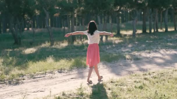 Uma mulher bonita nova está marrily andando ao longo da estrada na floresta entre as folhas, brilhando na luz solar — Vídeo de Stock