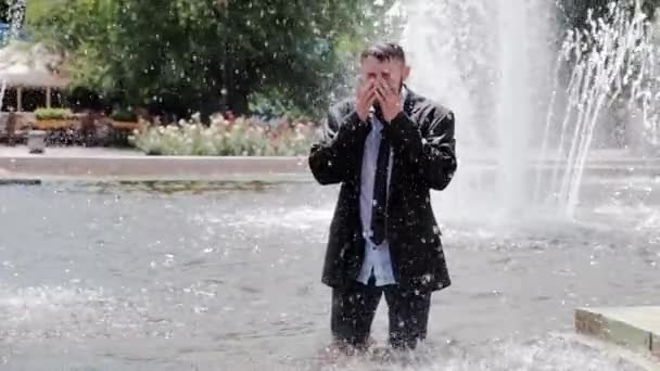 Un hombre está caminando en una fuente, cubriéndose la cara con las manos y sintiendo toda la tristeza del mundo — Vídeo de stock