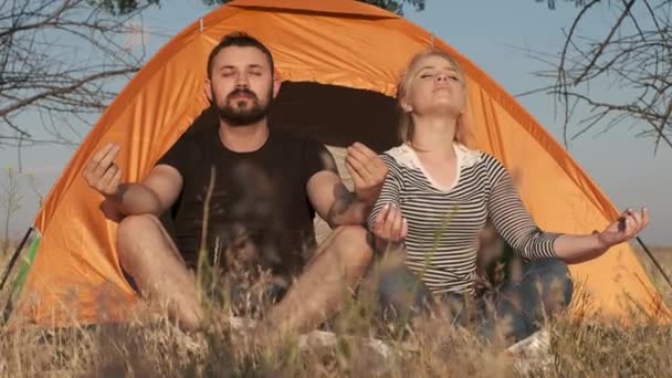Una pareja está meditando delante de una tienda de campaña, respirando tranquila y liberada — Vídeo de stock