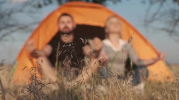 Um casal em um fundo está meditando na frente de uma tenda, respirando calmo e liberado contra o chão na frente — Vídeo de Stock