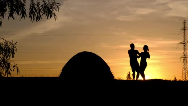 Uma silhueta de um casal amoroso girando em volta, de mãos dadas contra o pôr do sol — Vídeo de Stock