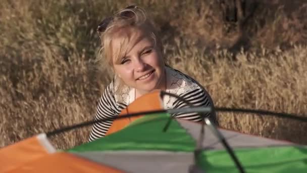 En ung kvinna på en bakgrund är leende och taliking medan du tittar på ett tält — Stockvideo