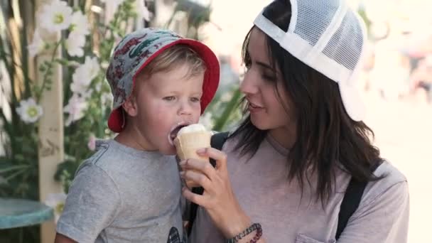 Μια στοργική μητέρα τρέφεται το παιδί με ένα παγωτό. Ένα μικρό αγόρι τρώει ευτυχώς, έχοντας υψηλά πνεύματα και το πρόσωπο του βρώμικου — Αρχείο Βίντεο