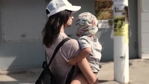 Egy fiatal gyönyörű nő hordozza szeszélyes gyermeke, mosolyogva, és mutat valami érdekes — Stock videók