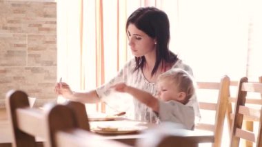 Bir sevgi ve bakım anne oğluyla masada oturup çocuğunu beslemeye çalışıyor. O başarısız olarak kendini bir şey yiyor.
