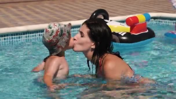 妈妈亲吻她的孩子, 和他一起在游泳池里玩耍。 — 图库视频影像